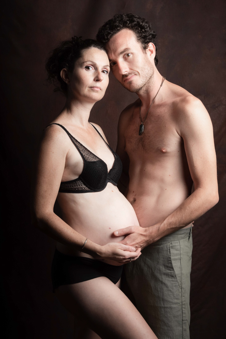 un couple pose lors d'une seance photo grossesse, lui dit un mot d'amour dans l'oreille