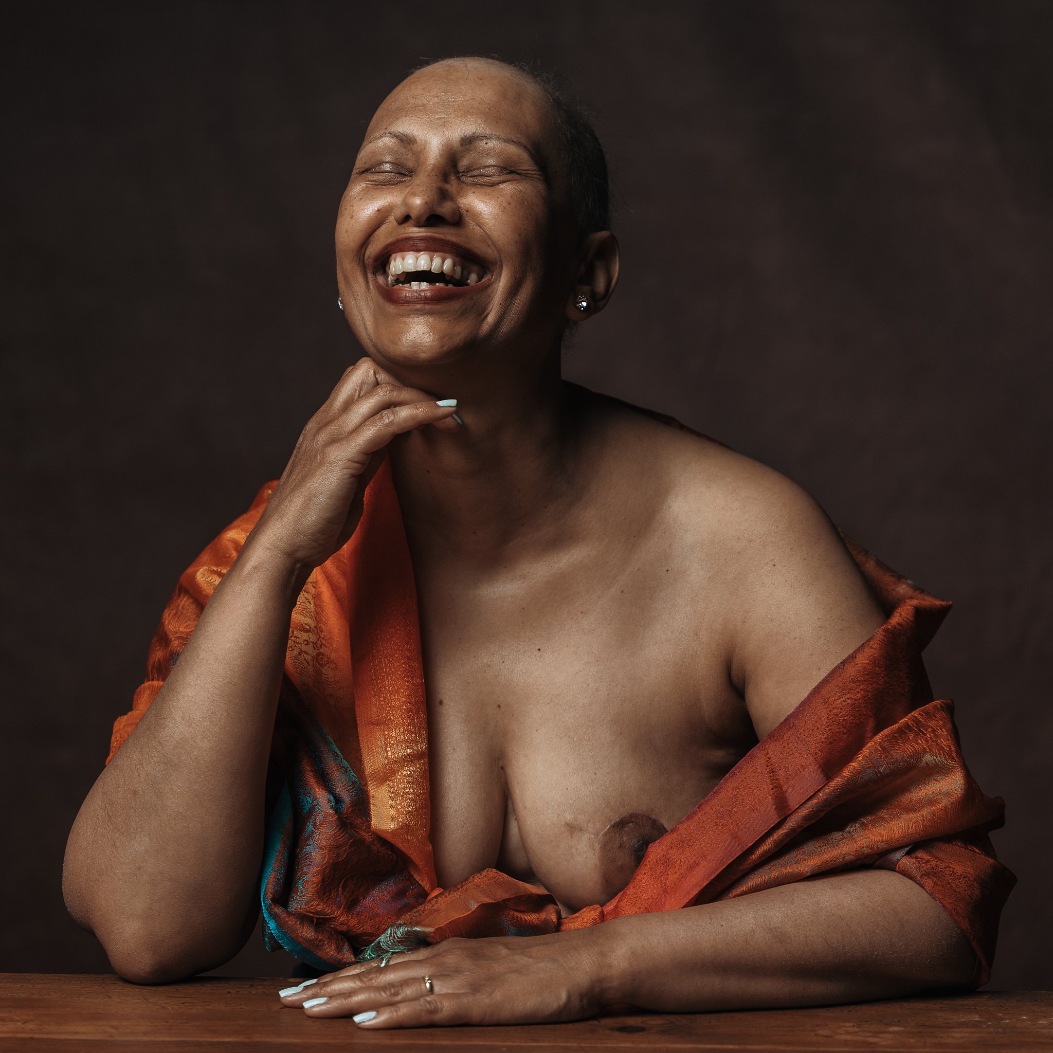 une femme appuyé sur la table, elle rit, une femme qpose en s'amusant, seance photo pour lutter contre le cancer du sein