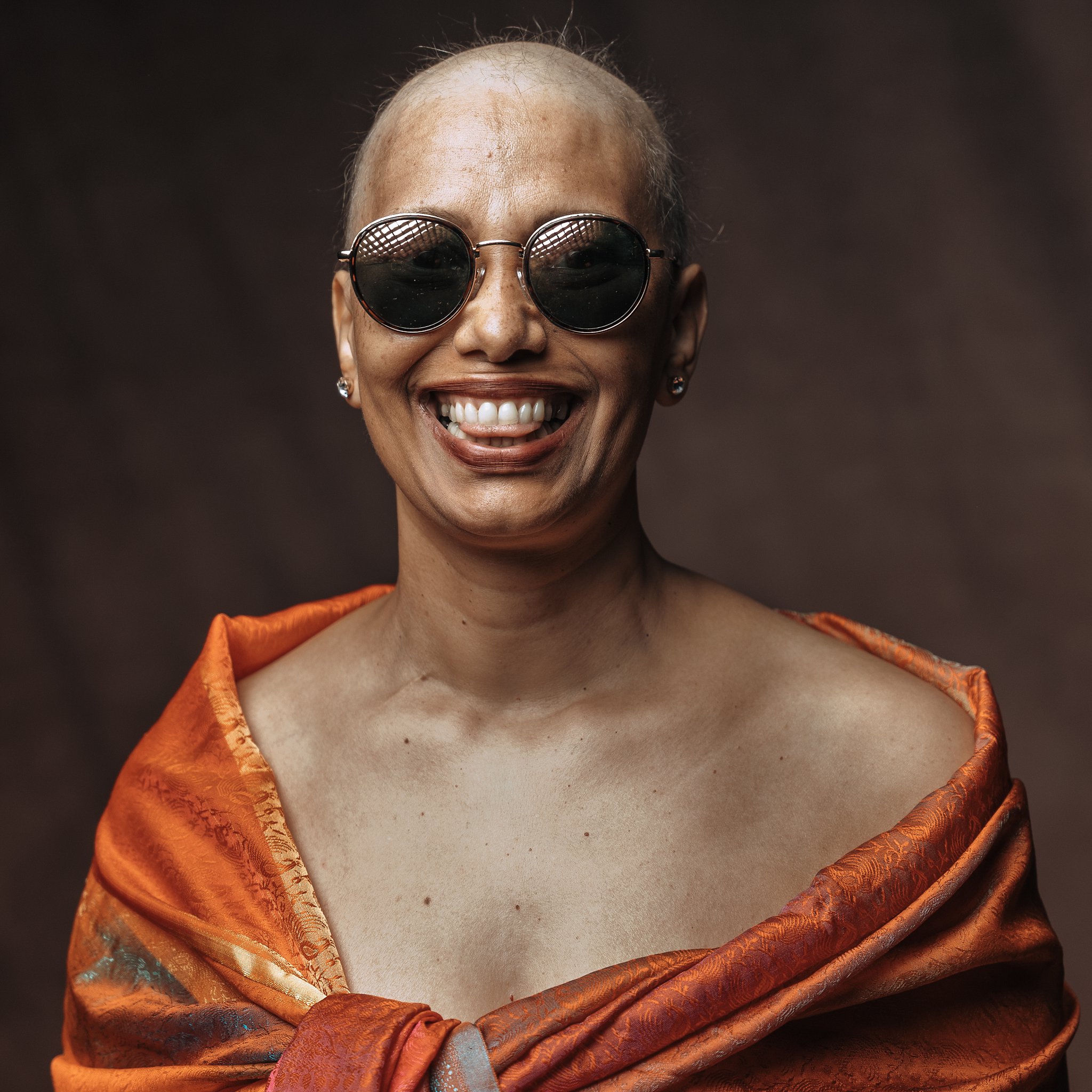 un portrait d'une femme, elle sourit et à des lunettes de soleil, une femme qpose en s'amusant, seance photo pour lutter contre le cancer du sein