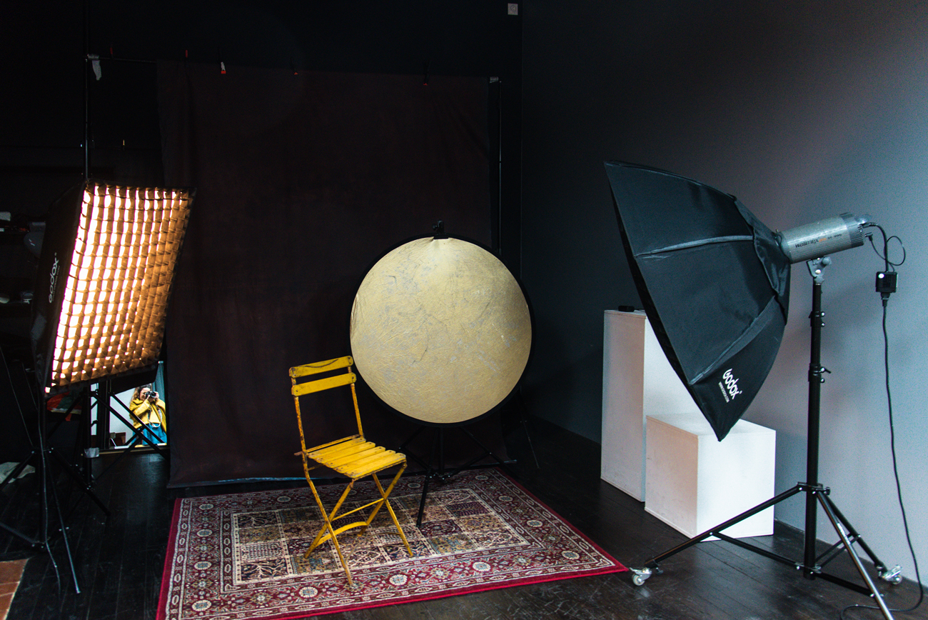 Configuration de studio photo à Rennes avec équipement professionnel prêt pour une séance photo. La scène montre une chaise jaune placée sur un tapis décoratif, entourée de lumières de studio et d'un réflecteur doré. L'arrière-plan sombre et le matériel de haute qualité sont mis en place pour capturer des portraits sophistiqués et créatifs. Cette photo illustre la préparation minutieuse et les outils utilisés pour garantir des portraits photo professionnels dans un cadre de studio à Rennes.