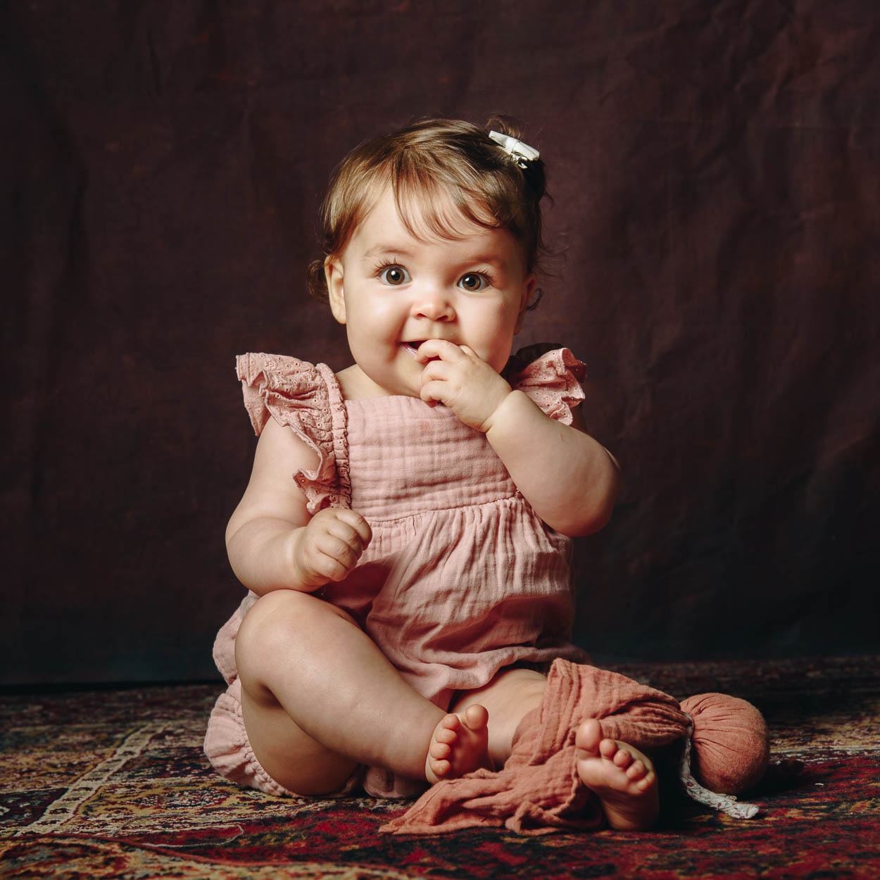 seance-photo-bebe-rennes Bébé assis en tenue rose lors d’une séance photo au studio Frédérique Jouvin à Rennes, capturé dans une lumière douce et naturelle.